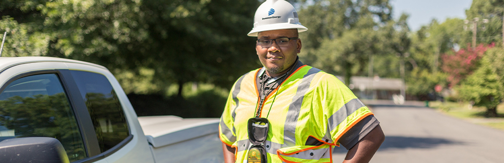 Dominion Energy employee in a hard hat stands, hands on hips, beside a truck