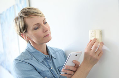 Woman consulting phone while adjusting thermostat